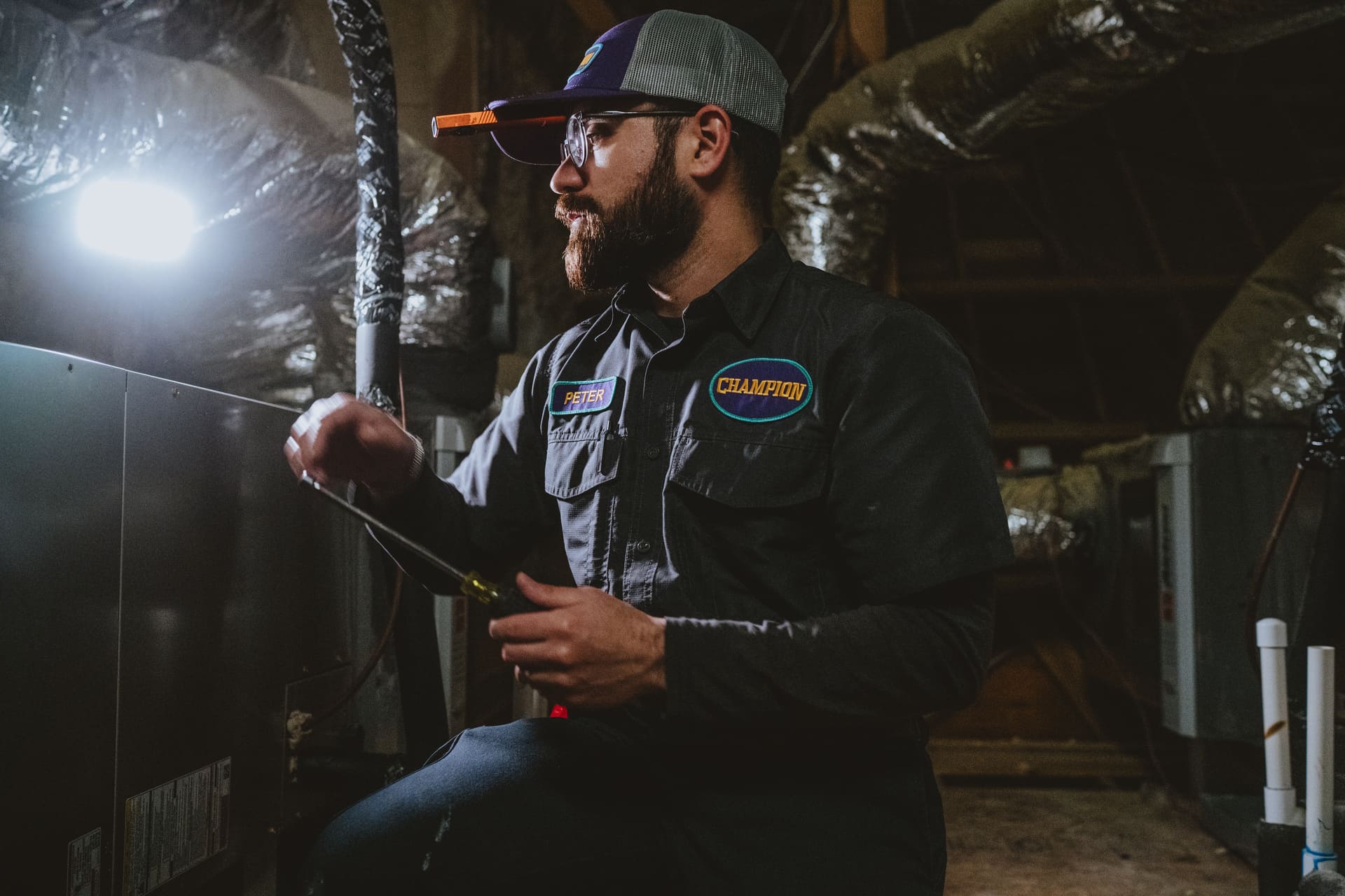 Champion technician working on an indoor HVAC unit surrounded by insulated ductwork.